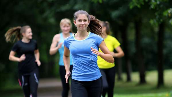 4 jugendliche Mädchen joggen auf einem Weg. Der Weg ist von Bäumen umgeben.